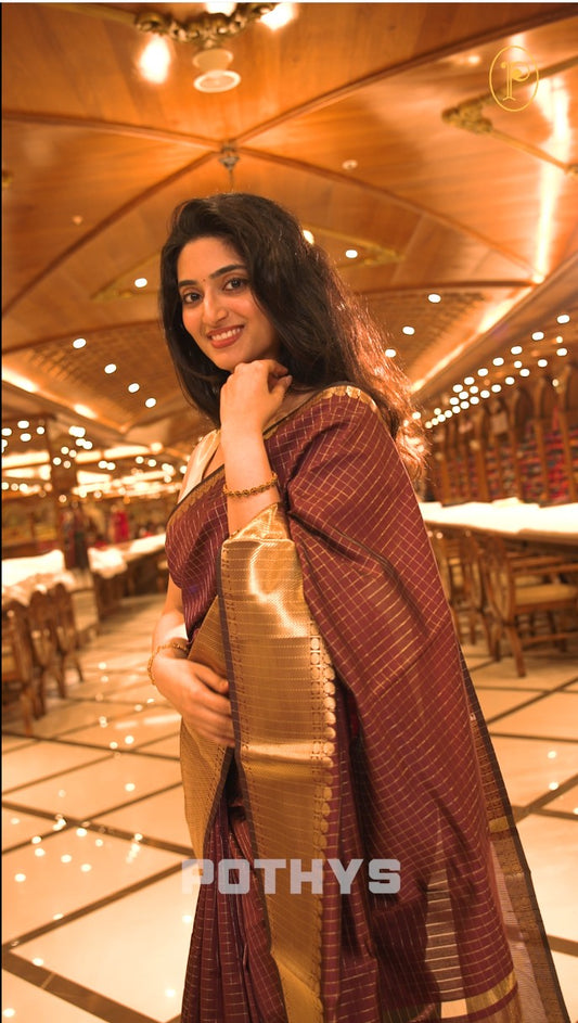 Dark wine colour semi banaras lichi silk saree featuring checked patterned body, complemented by gold zari border, paired with matching blouse piece.