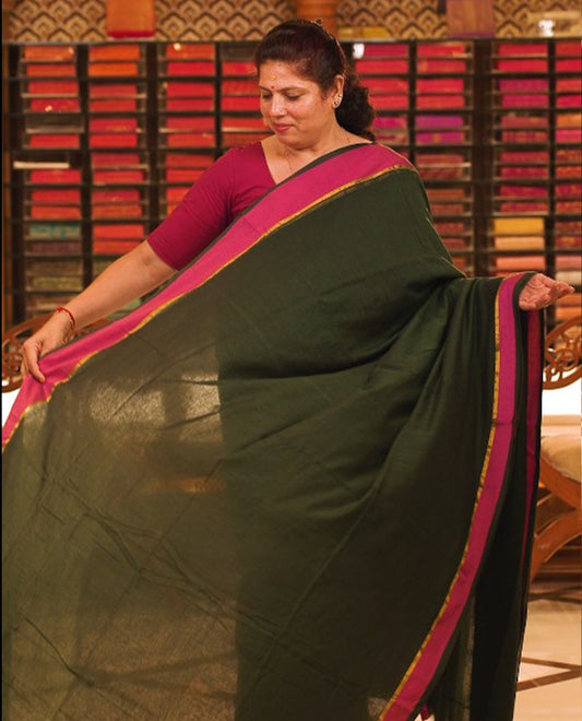 Bottle green colour Mul Cotton saree featuring a simple plain body with a contrast border, offering a classic and elegant look. Comes without a blouse piece.