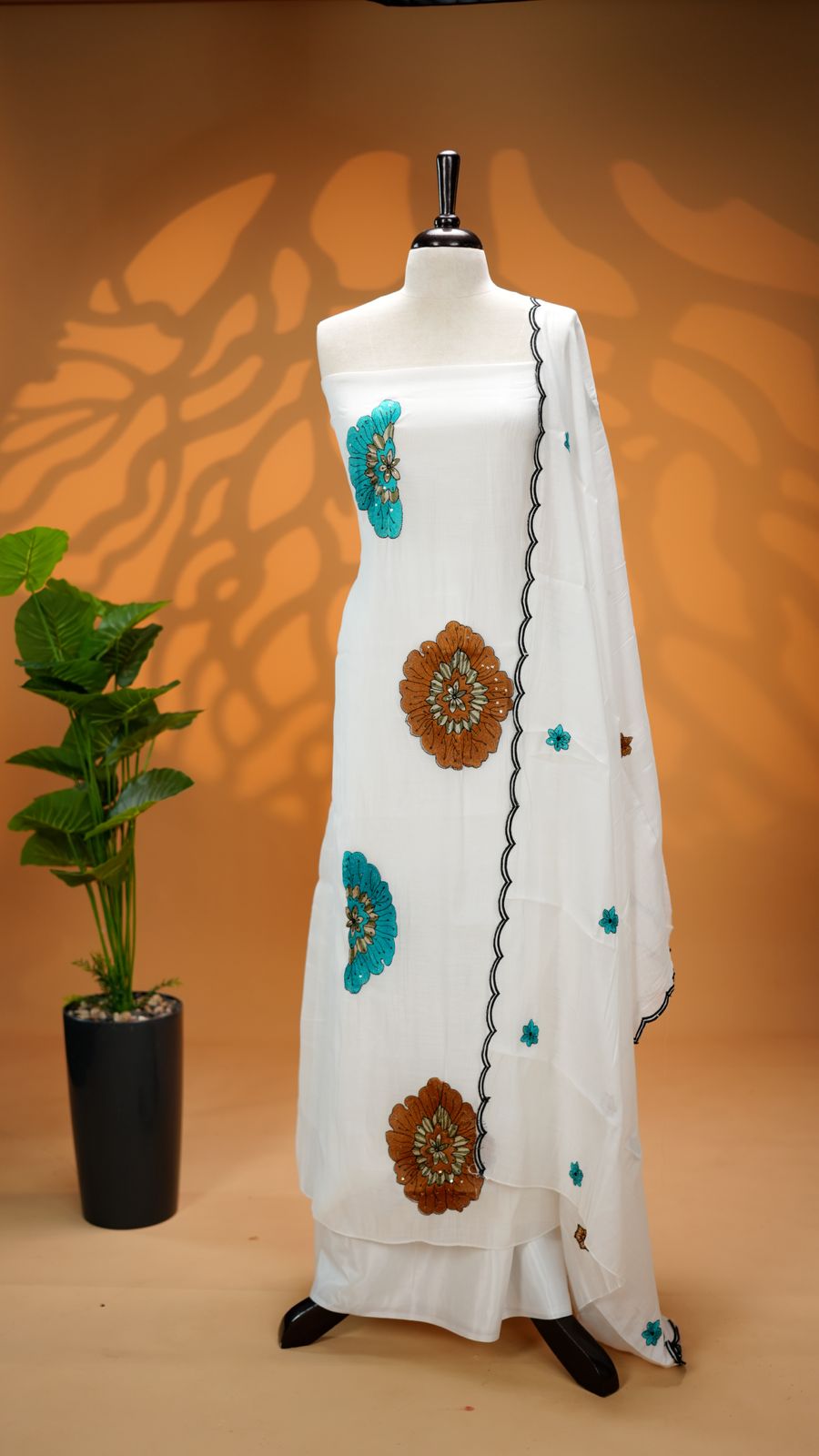 White Colour Mul Chanderi Salwar Material Featuring Peach Colour Floral Thread Work on body, paired with matching santoon Material Bottom & Floral thread Worked motifs And Scallop Embroidery Black Border Dupatta.