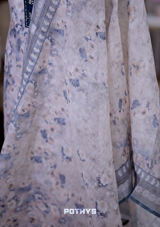 Off white colour jute cotton salwar material with blue leaf prints, featuring embroidery and mirror work on the neckline, paired with a printed dupatta and a contrast blue bottom for a graceful and elegant look.