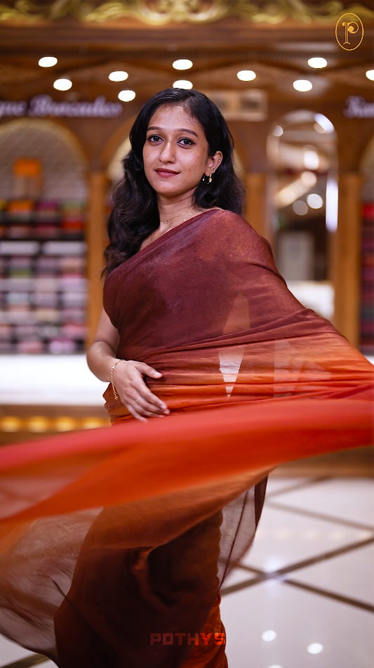 Brown orange colour saree with a soft textured body in deep orange, a rich pallu blending brown hues, and a subtle, seamless border for a graceful and contemporary drape & Comes with a matching blouse.