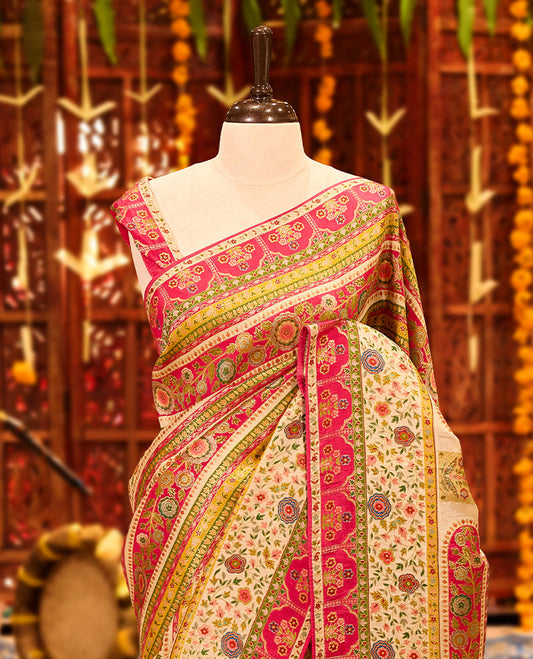 Ivory colour Pashmina silk saree richly adorned with intricate multicolour floral motifs across the body, accentuated by vibrant pink and green ornamental borders and a grand storytelling pallu, beautifully paired with a matching blouse piece.