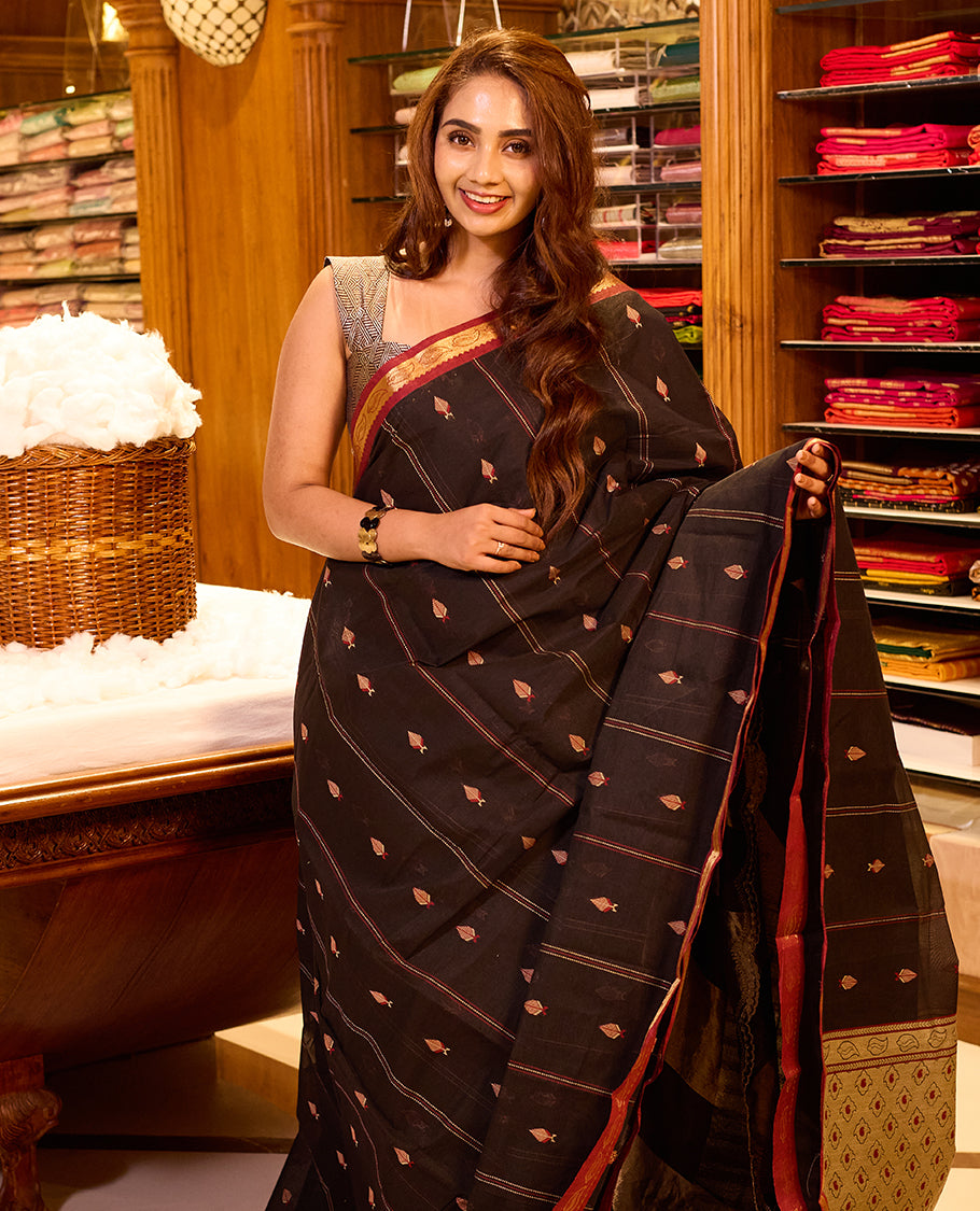 Dark Maroon colour Coimbatore cotton saree featuring subtle woven motifs across the body, paired with a contrast maroon pallu highlighted by a gold zari border, paired with a matching blouse piece.