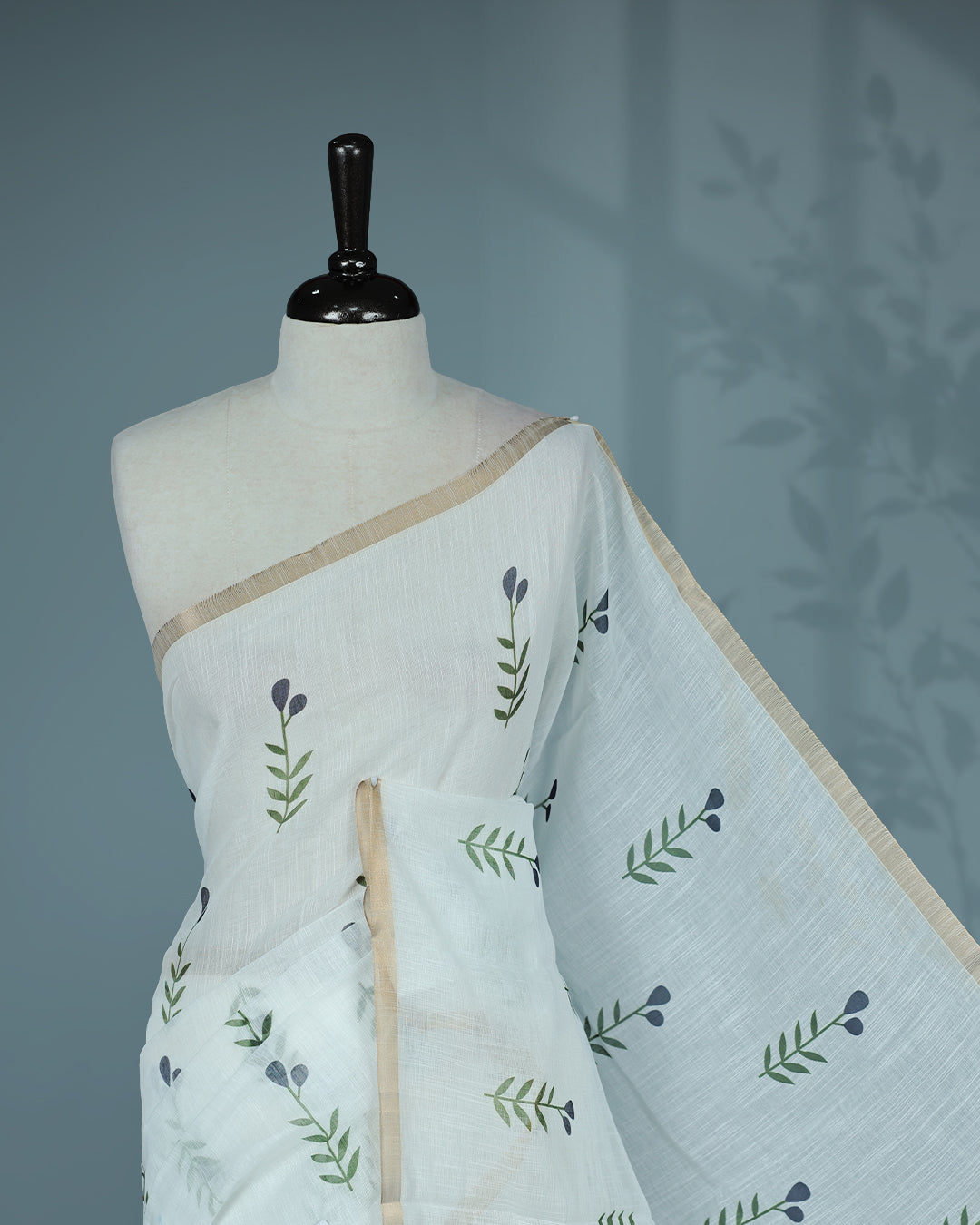 Off-white linen saree featuring beautiful Blue floral and leafy prints on the body, complemented by a tissue piping border and a contrasting pallu. Paired with a matching blouse piece.
