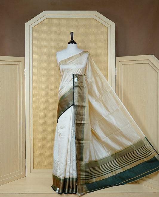 Cream colour semi Tussar silk saree featuring  Elegant body, Complemented by contrast Bottle Green with rich zari detailed for onam special, paired with contrast Blouse for Festive look.