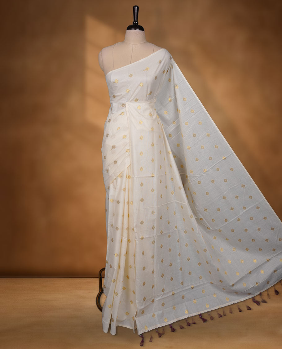 Off-white colour cotton Kerala saree featuring delicate gold butti motifs across the body and pallu, finished with a subtle gold border and tasselled pallu, paired with a matching blouse.