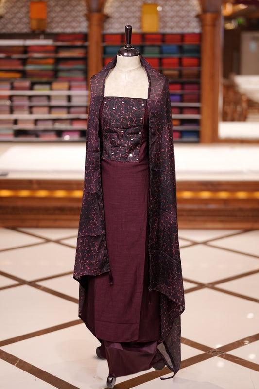 Maroon colour semi silk salwar material featuring subtle mirror work on the top, paired with a plain matching bottom & The set is completed with chiffon dupatta adorned with golden abstract prints for a classy finish.
