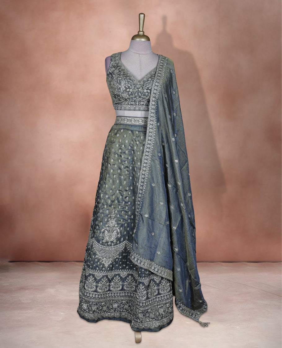Steel grey and olive ombre effect lehenga set with stitched sleeveless V‑neck embroidered blouse, matching stitched flared lehenga featuring heavy zari and sequin work, and coordinated dupatta with embellished border.